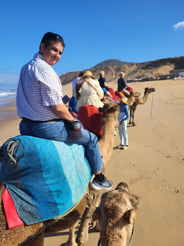 Miguel on a camel during an excursion across a sandy landscape in Morocco