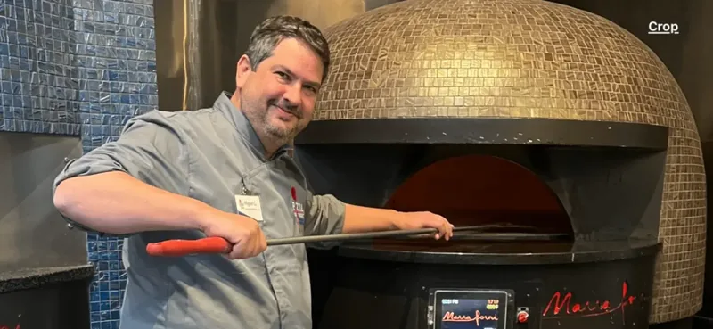Miguel working with a peel beside a wood-fired pizza oven
