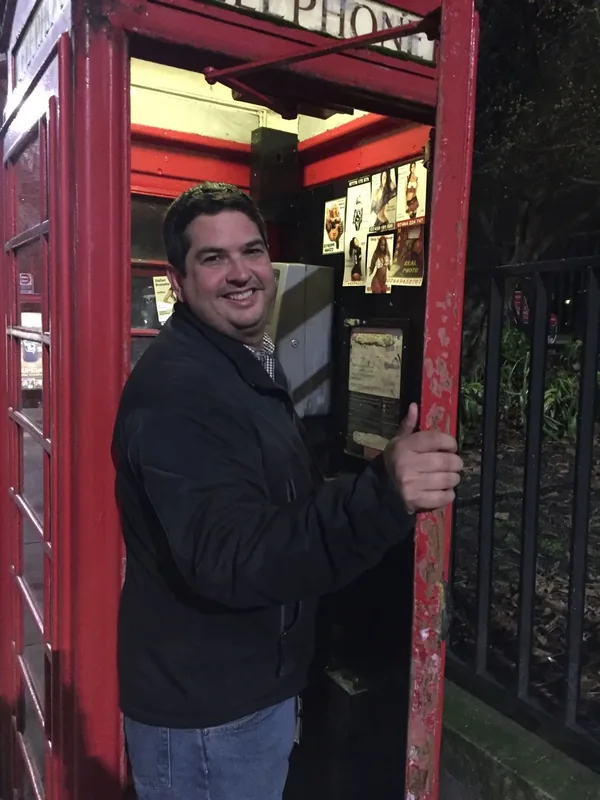 Miguel pausing beside a red phone booth during a travel moment
